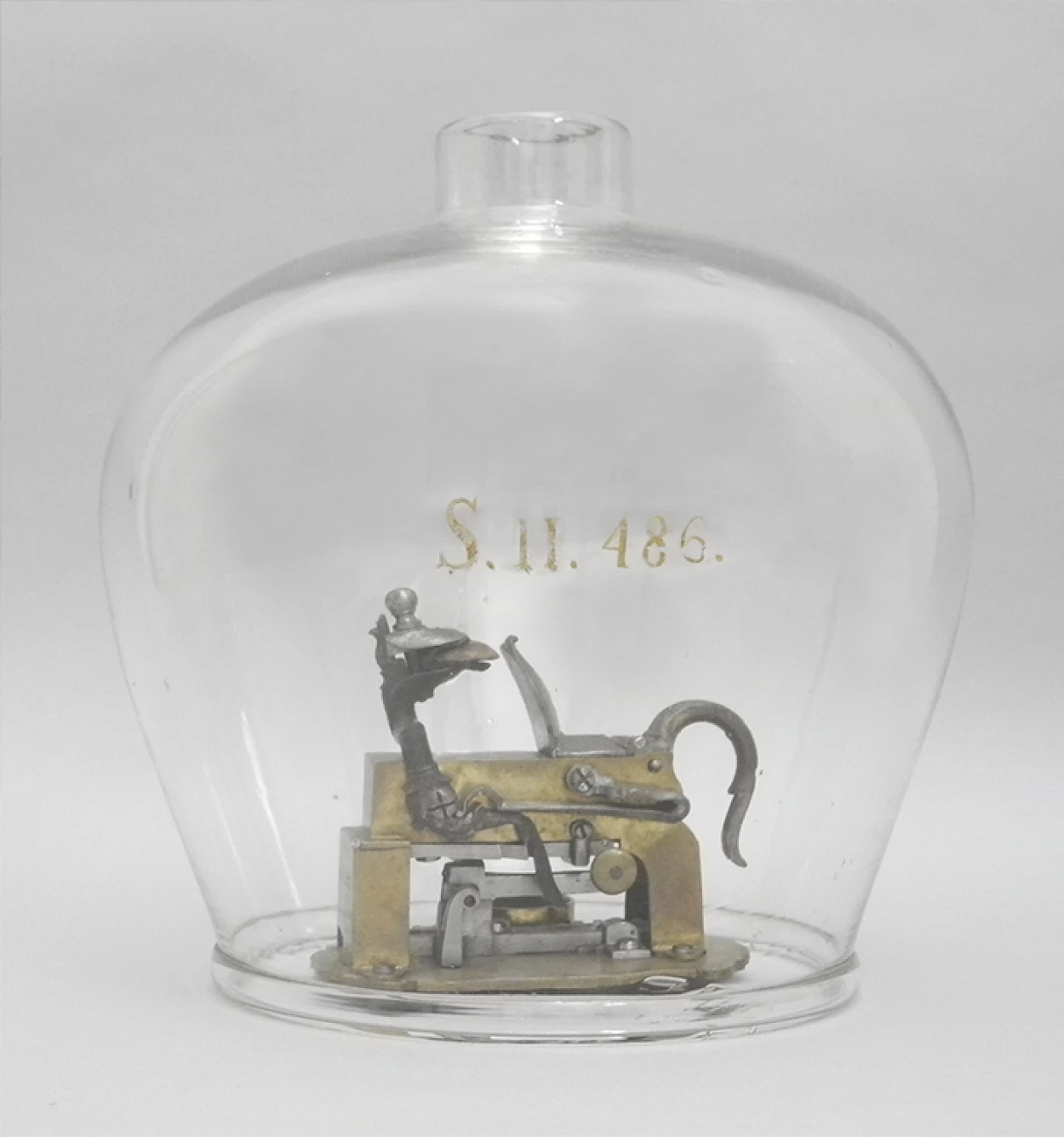 Fig. 2 - Disparador de pederneira no interior de uma campânula. No Index Instrumentorium esta campânula possui o número “S.II.486”. Este número encontra-se pintado a ouro na superfície de vidro. O número atual da campânula é o FIS.0511.